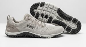 A pair of light grey Xero Shoes with branding on the side; one shoe is upright, the other on its side displaying a black and white textured sole—designed for walking and all-day comfort with a visible tread pattern.