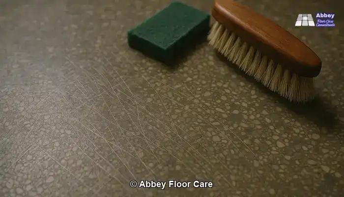 Scratched terrazzo floor with abrasive pads and brushes nearby.